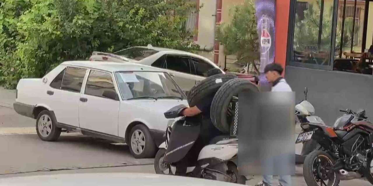 Otomobil lastiğini boynuna asan kuryenin ilginç taşıma yöntemi kameraya yansıdı